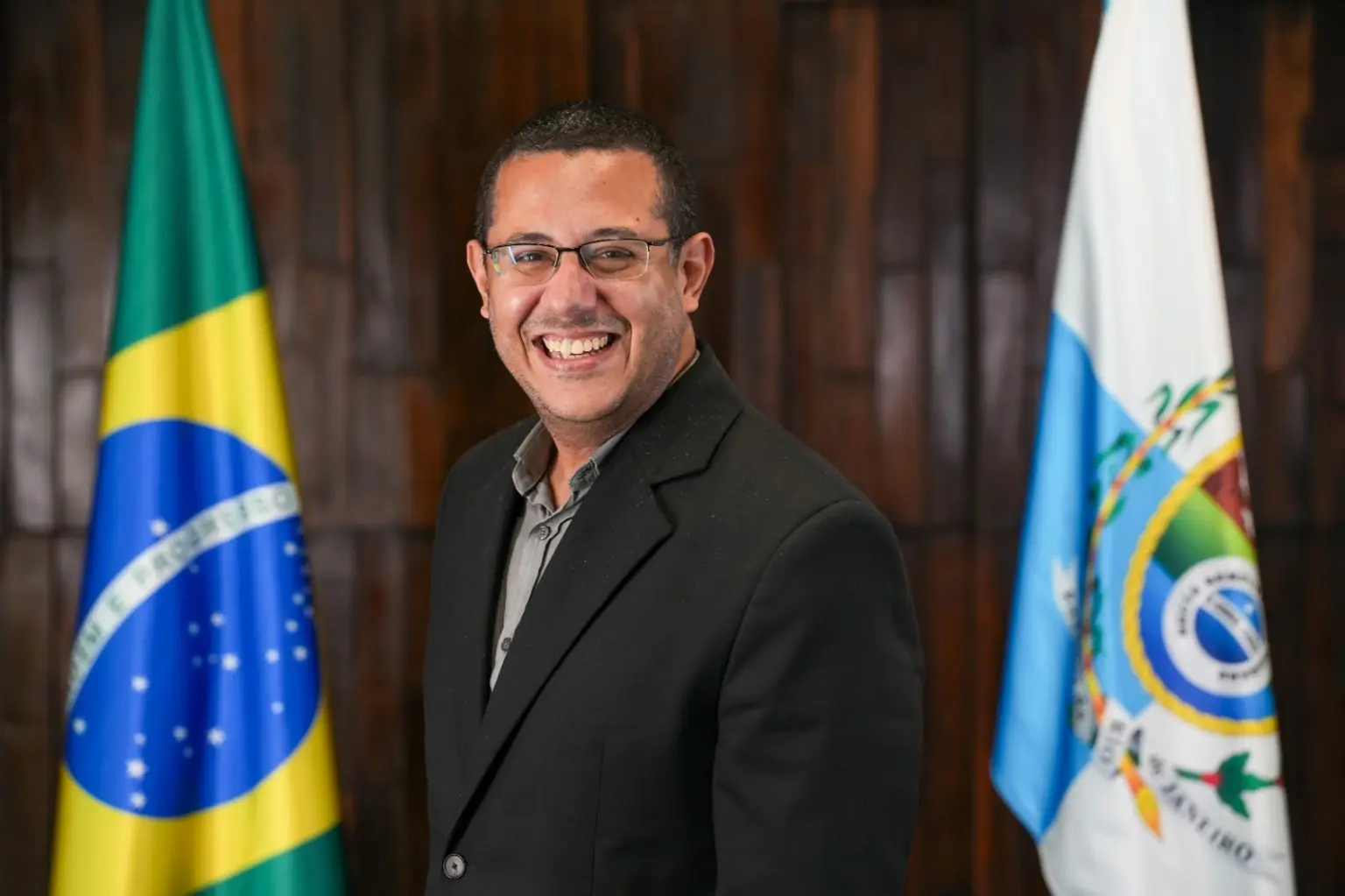 Alex Campos sorrindo, vestindo blazer preto